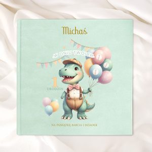 Okładka książki z obrazkiem uroczego dinozaura trzymającego balony w pastelowych kolorach, z napisem 'Michaś w dniu twoich 1 urodzin' oraz informacją 'Na pamiątkę Babcia i Dziadek' na tle miętowej okładki.