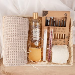Kosz upominkowy zawierający szampon Tesori d'Oriente, naturalny żel do kąpieli, wkładki bamboo, dwie probówki z solą i płatkami kwiatów, kawałek mydła oraz miękki ręcznik w jasnym kolorze na tle jasnej tkaniny.