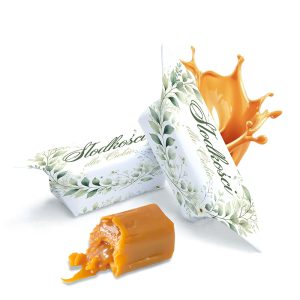 Dwie paczki cukierków o nazwie 'Słodkości dla Ciebie' na białym tle, z liściastym wzorem, z jedną paczką otwartą i widocznym złotym cukierkiem, z którego wycieka karmel, oraz tło z kroplą karmelu w ruchu.
