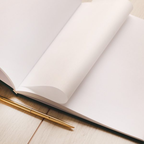 Pusty notes w białymi kartkami, z jedną stroną lekko zawiniętą, obok złota długopis na drewnianym stole.