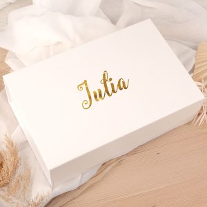 Biała pudełko z delikatnym złotym napisem "Jutia" na pokrywie, otoczone jasnymi tkaninami i naturalnymi dodatkami w tle.