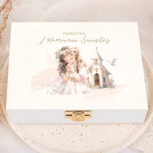 Biała skrzynka z ilustracją dziewczynki w białej sukience modlącej się, z kwiatową opaską na głowie, obok malutkiego kościoła i gołębia; napis na wieczku głosi 'Pamiątka, I Komunii Świętej'.