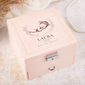Różowa szkatułka z rysunkiem śpiącego dziecka na wieczku, imieniem "LAURA" oraz datą 21/06/2026, z zapisanymi wagą 3540g, długością 51cm i godziną 9:25, umieszczona na jasnym tle z biżuterią w tle.