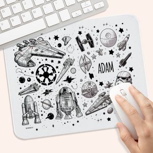 Podkładka pod mysz w stylu sci-fi z rysunkami statków kosmicznych, planet, gwiazd oraz postaci, z widocznym imieniem 'ADAM' na białym tle; w rogu widać rękę trzymającą mysz komputerową i kawałek klawiatury.