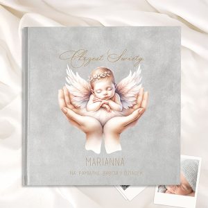 Okładka albumu z ilustracją przedstawiającą zaspaną niemowlęcą wróżkę z różowymi skrzydłami, trzymaną w dłoniach. Na okładce widnieje napis 'Chrzest Święty' oraz imię 'MARIANNA' z dedykacją 'na pamiątkę, babcia i dziadek'. Tło w odcieniu szarości.