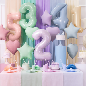 Kolorowe balony ułożone w kształcie cyfr i gwiazd, z pastelowym wystrojem stołu na przyjęcie urodzinowe, zawierającym torty, kadzidełka oraz ozdoby w różnych kolorach.