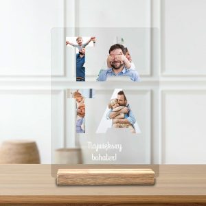 Przezroczysta tablica z wydrukowanym napisem 'Największy bohater!' i obrazami przedstawiającymi ojca z dziećmi, umieszczona na drewnianej podstawce, z jasnym tłem i stylowym wykończeniem.