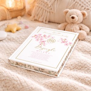 Książka w białej okładce z różowymi kwiatami, tytuł "Błogosławieństwa" oraz data "15 maja 2022", leży na miękkim kocyku obok pluszowego misia i dekoracyjnych przedmiotów.