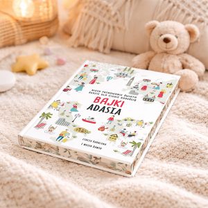 Książka 'Bajki Adasia' leży na miękkim dywanie, obok znajduje się pluszowy miś. Okładka książki jest ozdobiona kolorowymi ilustracjami, a na górze widnieje napis 'Niech poznawanie świata będzie dla ciebie radością'.