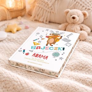 bajki-prezent-dla-przedszkolaka Książka z kolorową okładką z ilustracją zwierzęcia i napisem "BAJEJCKI ADAMA" na tle jasnego kocyka, obok pluszowy miś i różne dekoracyjne przedmioty, w przytulnym wnętrzu.