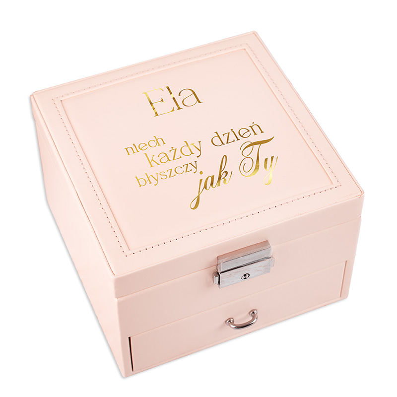 Różowa, kwadratowa szkatułka z napisem na wieczku, zawierającym imię 'Ela' oraz złotym tekstem: 'niech każdy dzień błyszczy jak Ty'. Szkatułka ma metalowy zamek i małą szufladkę z przodu.