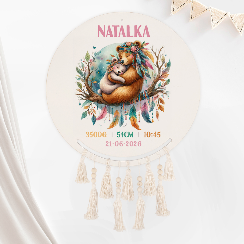 Okrągła ozdoba z rysunkiem niedźwiedzicy i jej młodego, siedzących na gałęzi w otoczeniu liści i piór, z napisem 'NATALKA' u góry, oraz danymi urodzinowymi: 3500G, 54CM, 10:45, 21-06-2026, z frędzlami u dołu.