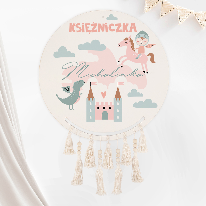 Okrągła dekoracja przedstawiająca różowe napisy "Księżniczka" i imię "Michalinka", z ilustracjami konia, smoka, zamku i chmur na jasnym tle, ozdobiona frędzlami na dole.