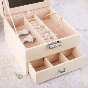 Pudełko na biżuterię w jasnym kolorze z oddzieleniami na pierścionki, kolczyki i inne akcesoria, z kluczykiem do zamykania.