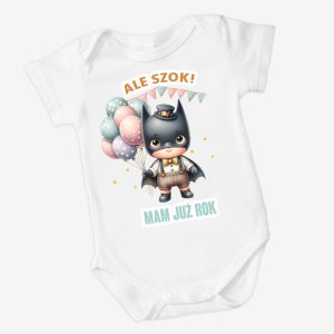 Biały body dziecięce z ilustracją małego superbohatera w czarnym kostiumie, trzymającego kolorowe balony, z napisem 'ALE SZOK!' i 'MAM JUŻ ROK' na przodzie.