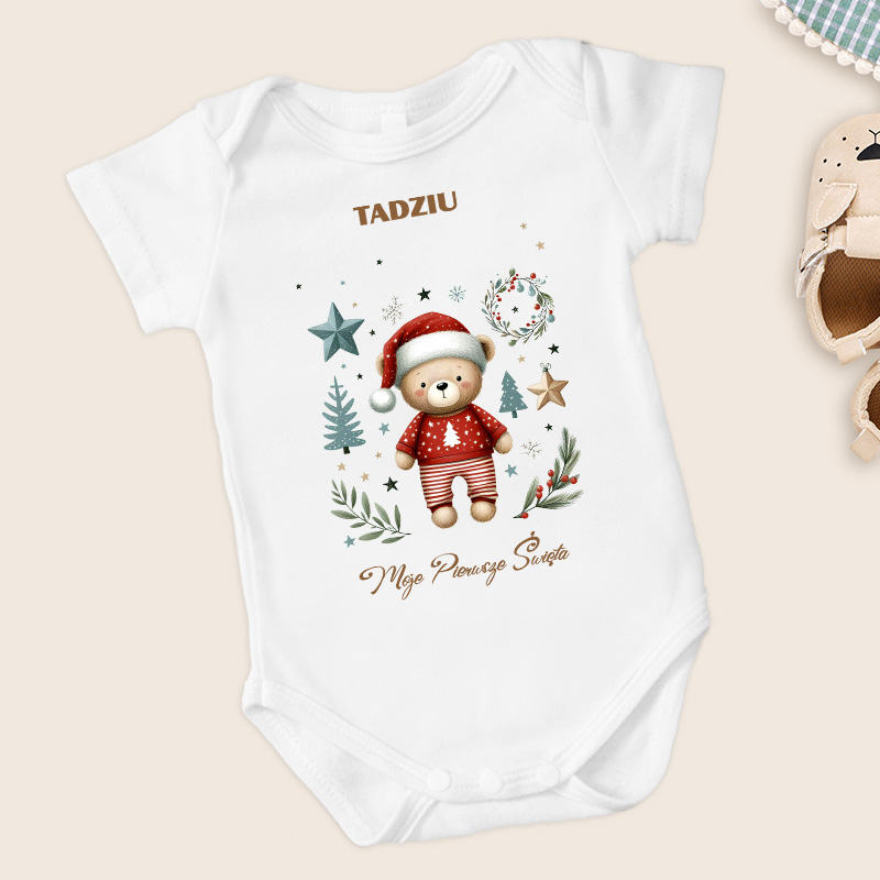 Biały body dziecięce z nadrukiem przedstawiającym pluszowego misia w czerwonym sweterku z choinką, w otoczeniu zielonych gałązek, gwiazdek oraz tekstem "TADZIU" i "Moje Pierwsze Święta".