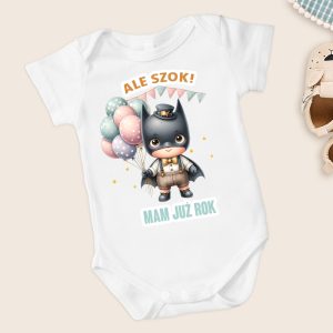 Biały body dla dzieci z ilustracją małego superbohatera w czarnym kostiumie oraz kapeluszu, trzymającego kolorowe balony. Na koszulce napis: 'ALE SZOK!' i 'MAM JUŻ ROK'.