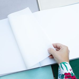 księga prezent dla dziewczynki grafika ubranka Osoba trzymająca jedną z białych stron otwartej książki, w tle widoczne są różnokolorowe kartki papieru.