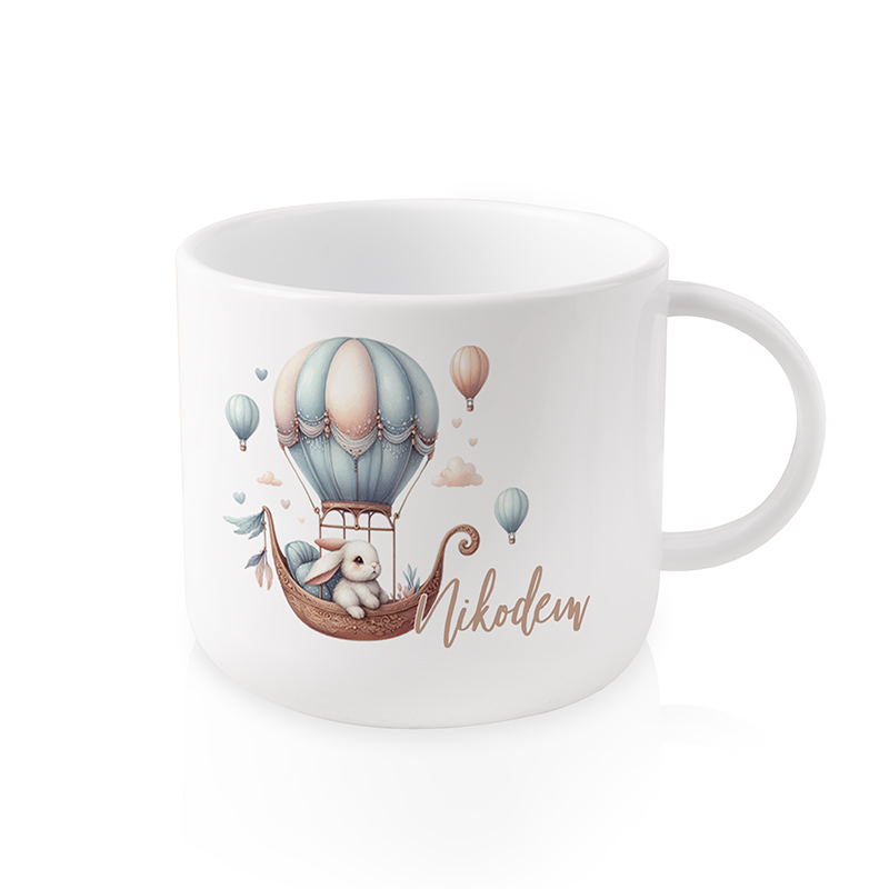 Biała filiżanka z ilustracją przedstawiającą balon na gorące powietrze i pluszowego króliczka, obok napis 'Nikodem'. Na filiżance znajdują się również kolorowe baloniki i chmurki w tle.