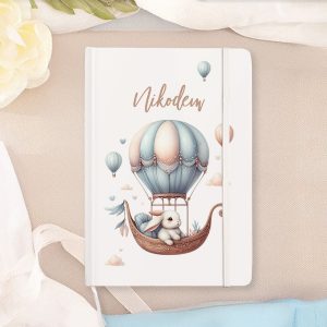 Notatnik z ilustracją przedstawiającą królika w balonie na gorące powietrze, otoczony chmurkami i balonami, z imieniem 'Nikodem' na okładce.