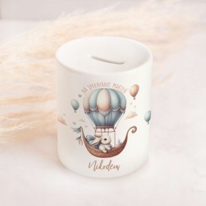 Biały skarbonka z rysunkiem balonu na ogrzane powietrze i króliczka siedzącego w łodzi, z napisem "NA SPEŁNIANIE MARZEŃ" i imieniem "Nikodem".