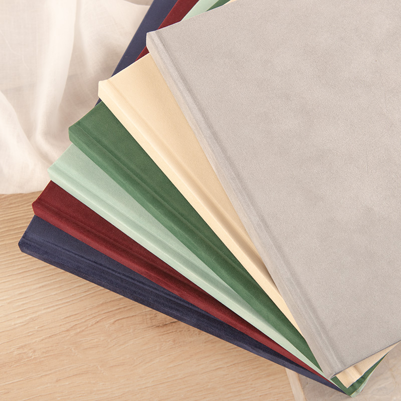 Zestaw kolorowych, gładkich okładek książek ułożonych w stosie, na tle jasnym z naturalnego drewna.