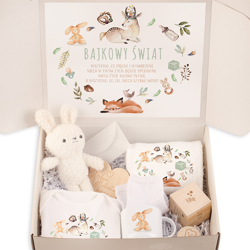 Zawartość pudła z prezentem dla dzieci, w tym biała pluszowa zabawka króliczek, ubranka z kolorowymi nadrukami zwierząt, drewniana kostka, oraz kartka z napisem 'Bajkowy Świat' i dekoracyjnymi ilustracjami przyrody i zwierząt.