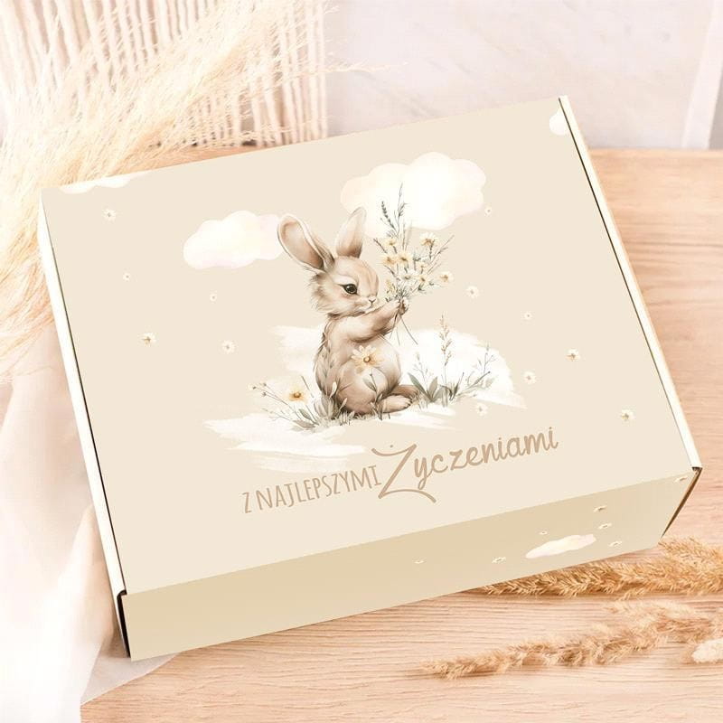Rózowa paczka z ilustracją uroczego królika trzymającego bukiet kwiatów, z napisem 'Z NAJLEPSZYMI ŻYCZENIAMI' w delikatnym stylu na tle jasnych chmur.