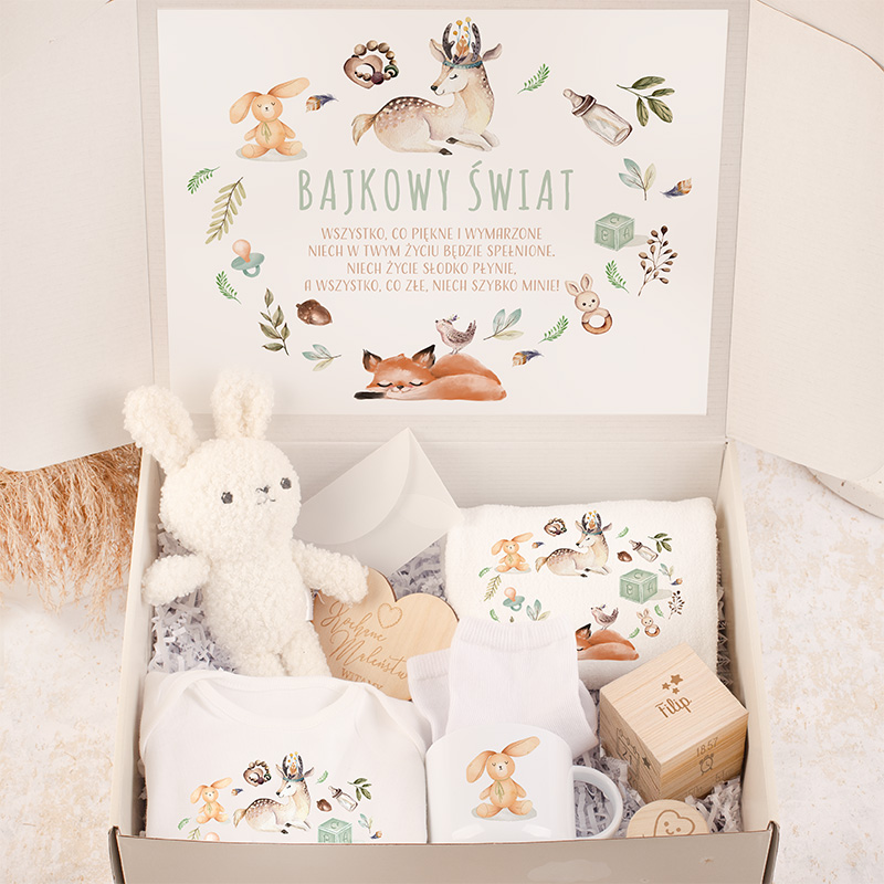 Zestaw prezentowy dla dziecka z białym pluszowym królikiem, ubrankami z kolorowymi nadrukami zwierząt, drewnianą kostką do zabawy oraz kartką z napisem 'Bajkowy Świat' i ilustracjami leśnych zwierząt.