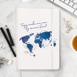 Notes z kolorową mapą świata, napis 'Twoja wiedza ma moc, by zmienić Świat' oraz mały samolot; znajduje się na biurku z przyborami biurowymi i filiżanką herbaty.