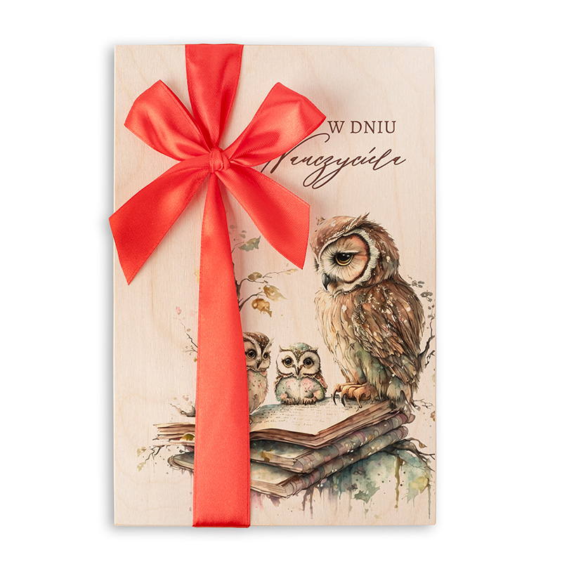 Drewniane opakowanie z ilustracją sowy oraz dwóch małych sów, z wstążką w kolorze czerwonym, na tle ciepłego odcienia drewna, z napisem 'W DNIU WIECZYCIA'.