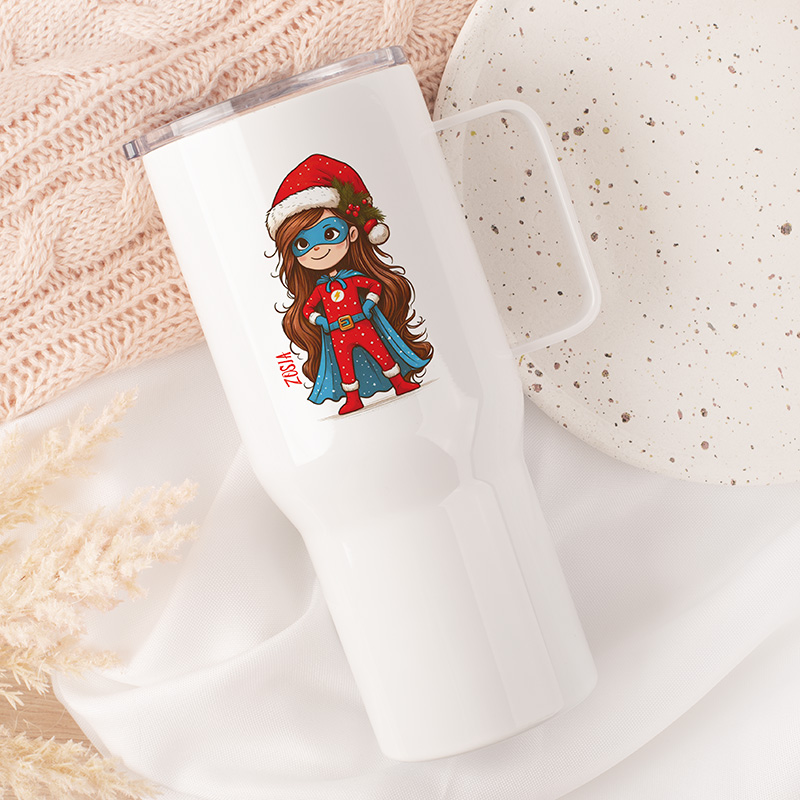 Biały kubek termiczny z rysunkiem dziewczynki w kostiumie superbohatera, noszącej niebieski płaszcz i czerwoną czapkę z pomponem, na tle miękkiej, różowej dzianiny i talerza z drobnym wzorem.