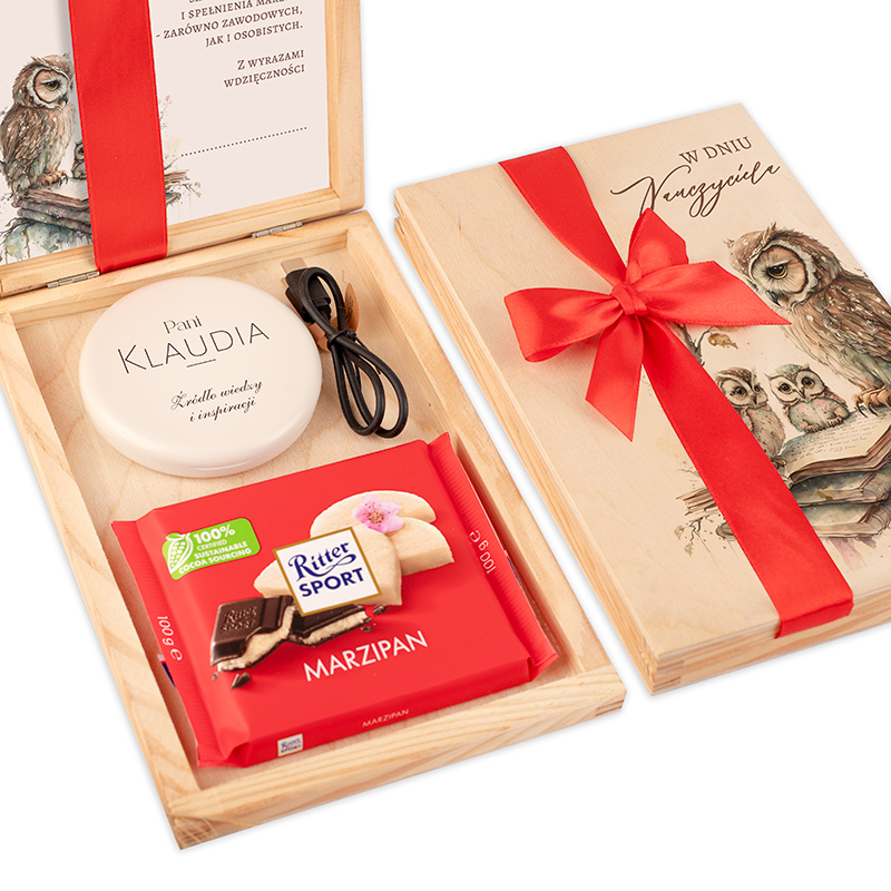 Ekskluzywne drewniane pudełko z czerwoną wstążką, wewnątrz prezent znajdują się kosmetyk oraz czekolada Ritter Sport o smaku marcepan; widoczne także ilustracje ptaków na wewnętrznej stronie pokrywki.