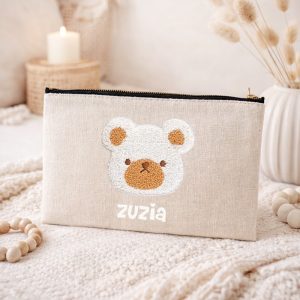 Kosmetyczka w kolorze jasnoszarym z haftowanym wizerunkiem misia oraz imieniem "Zuzia" na przodzie.