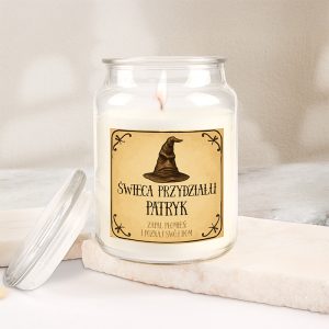 Świeca w szklanym słoiczku z etykietą, na której znajduje się graficzny wizerunek czapki oraz napisy "Świeca przydziału Patryk" i "Zapal płomień i poznaj swój dom". Słoiczek stoi na jasnym podłożu, a w środku świeca jest zapalona.