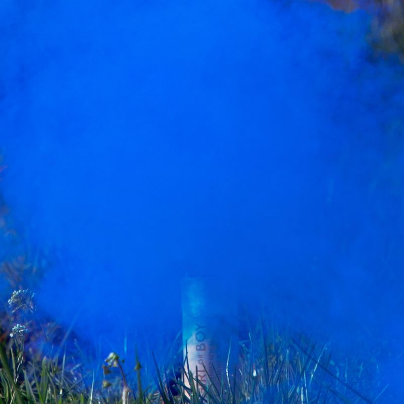 A can partially obscured by vibrant blue smoke, surrounded by green grass and a few small white flowers.