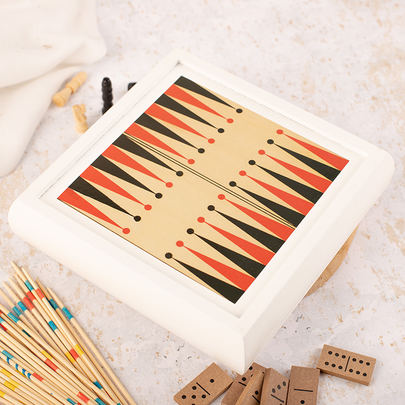 Stół do gry z ozdobnym wzorem w czarne i czerwone trójkąty, otoczony elementami gier, takimi jak domino i patyczki do gier na jasnym tle.