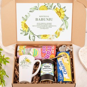 Zamknięta kartonowa pudełko z napisem 'Kochana Babuniu', zawierające filiżankę, herbatę, chałwę, słodycze i akcesoria do parzenia herbaty, otoczone wypełnieniem w kolorze brązowym.