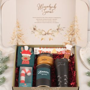 Wnętrze ozdobnego pudełka z prezentami na Święta, zawierające skarpetki z motywem renifera, miód w słoiku, czarny kubek, herbatę, świąteczną czekoladę, oraz ozdobę w kształcie piernika; wieczór Bożego Narodzenia w tle z dekoracjami, napis "Wesołych Świąt" na wieczku.