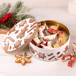 Otwarta puszka z różnorodnymi słodyczami, w tym cukierkami i ciastkami, ozdobiona motywami świątecznymi, z lukrowanym piernikiem w kształcie płatka śniegu obok.