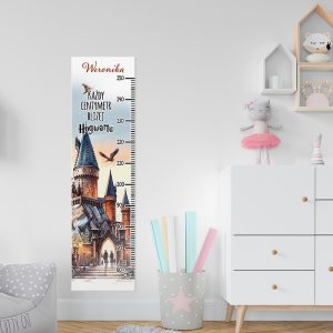 Wysokościomierz z wizerunkiem zamku, na którym widnieje napis "Każdy centymetr bliżej Hogwartu" oraz imię "Weronika", zawieszony na białej ścianie obok kolorowych kartek w pojemniku oraz miękkiego fotelika.