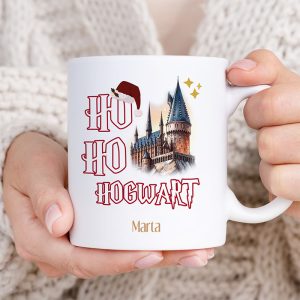 Osoba trzymająca kubek z napisem "HO HO HOGWART" oraz rysunkiem zamku z wieloma wieżami, ozdobionym czerwoną czapką Mikołaja i złotymi gwiazdkami; widoczna jest też imię "Marta" na kubku.
