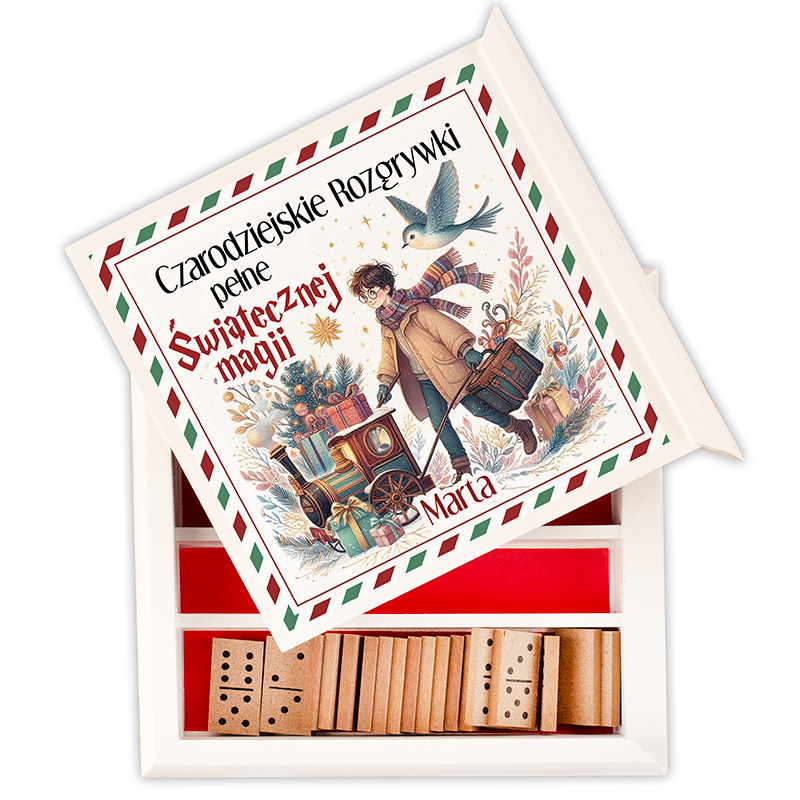 Otwarta drewniana skrzynka z grą planszową, z górnym wiekiem ozdobionym ilustracją chłopca z torbą podróżną i małym pociągiem wśród świątecznych dekoracji. Wewnątrz widoczne drewniane kostki do gry.