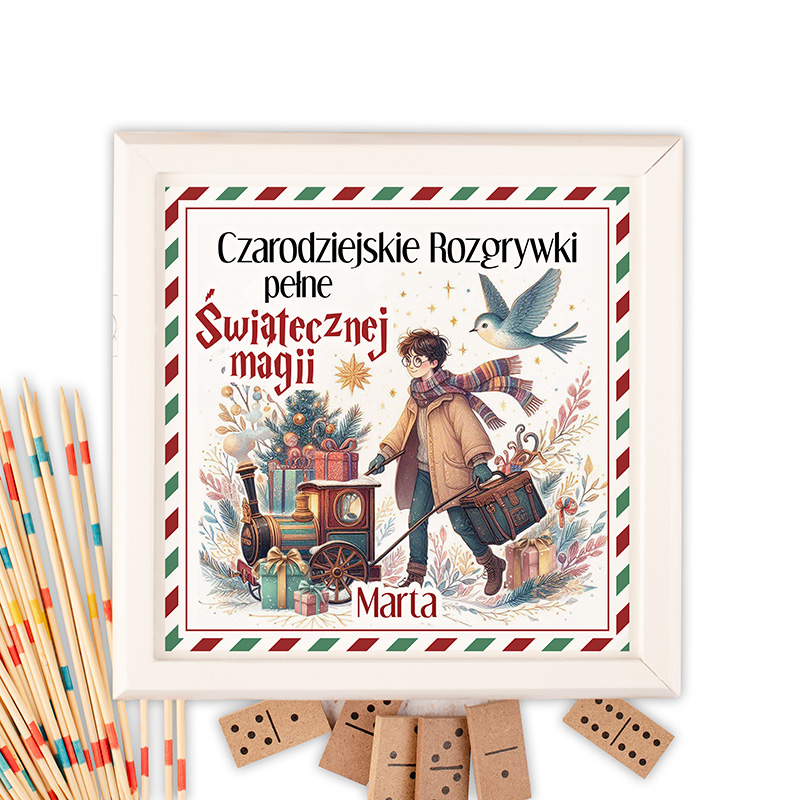 Grafika przedstawiająca kolorową ilustrację z dzieckiem ciągnącym mały pociąg pełen prezentów w zimowym otoczeniu. W tle widać choinkę i ptaka, a u góry widnieje napis 'Czarodziejskie Rozgrywki pełne Świątecznej magii' oraz imię 'Marta'. Obok znajdują się kolorowe patyczki oraz domino na stole.