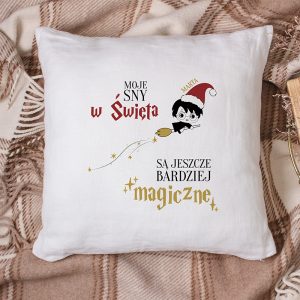 Poduszka z nadrukiem tekstu "MOJE SNY w Święta" oraz "SĄ JESZCZE BARDZIEJ magiczne", a obok postać w zielonym czapki mikołaja na miotle.