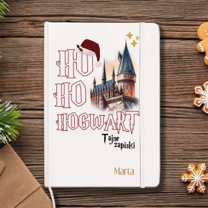 Okładka notatnika z napisem "Ho Ho Hogwarts" oraz ilustracją zamku, ozdobiona czapką Mikołaja i gwiazdkami, w otoczeniu gałązek świerku i dekoracji świątecznych.