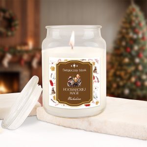 Słoik świecy zapachowej z etykietą "Świąteczny blask" i napisem "HOGWARCKIEJ MAGII" w ciepłej, przytulnej scenerii przy kominku i choince w tle.