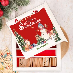 Zestaw gier świątecznych w białym pudełku, z czerwonym wieczkiem z ilustracją, na którym widać bałwana, sanki, choinki oraz zwierzątka, w tym wiewiórkę i renifera. Na wieczku znajdują się napisy "Rozrywki świąteczne" i "PODPIS". Wnętrze pudełka zawiera drewniane kostki domina.