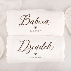Dwa białe ręczniki na jasnym tle, górny z napisem 'Babcia ♥ Jadwiga' w stylu kaligraficznym, dolny z napisem 'Dziadek ♥ Czesław', oba w brązowym kolorze.