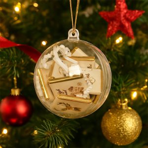 Przezroczysta bombka choinkowa wypełniona małymi, ozdobnymi pudełkami, z złotymi detalami, zawieszona na choince z rozmytymi światełkami i ornamentami w tle.